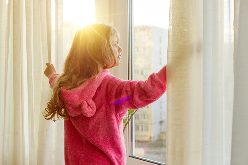 girl opening her curtains to a sunny day