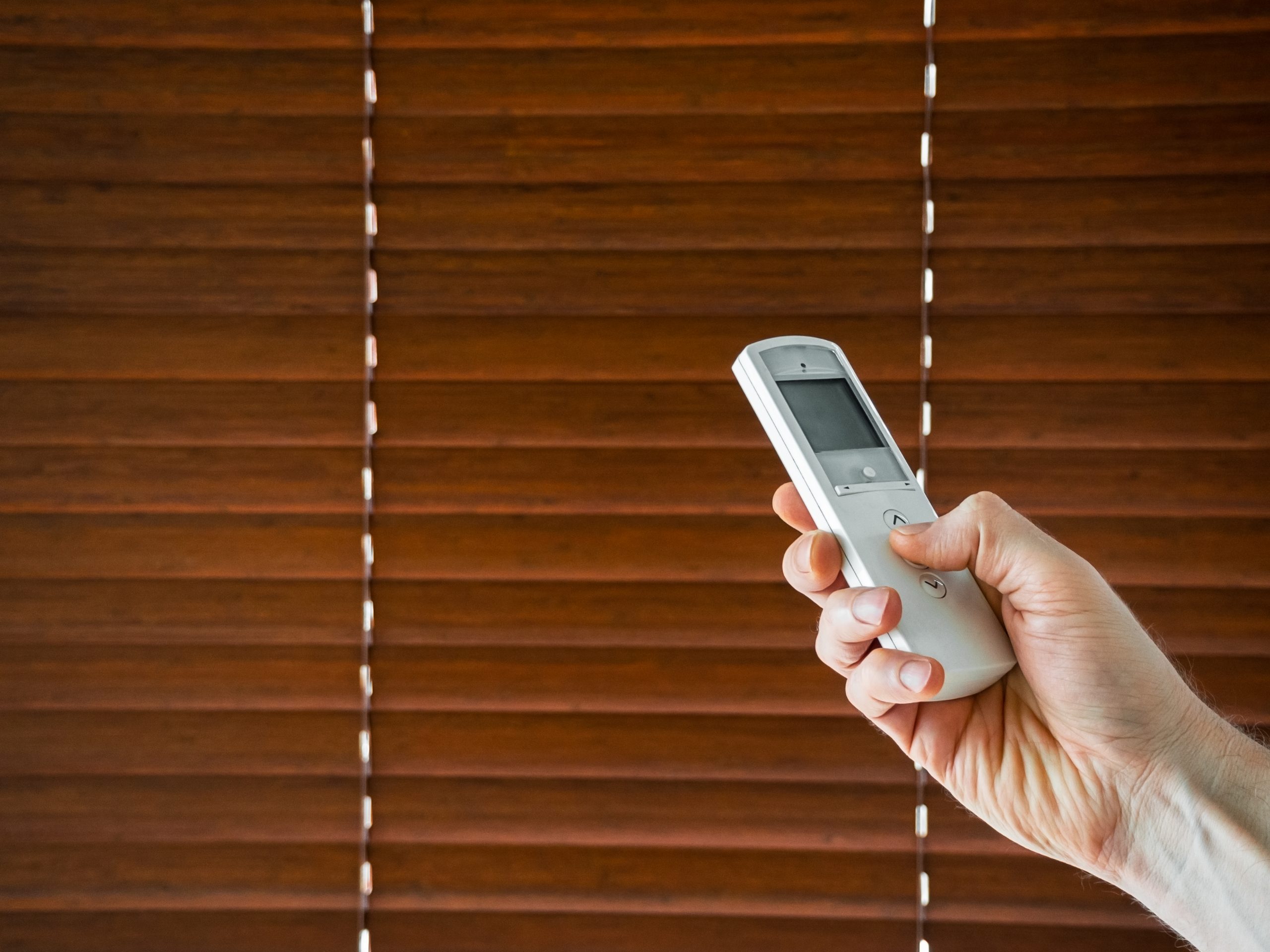 hand holding a remote control to open their electric blinds