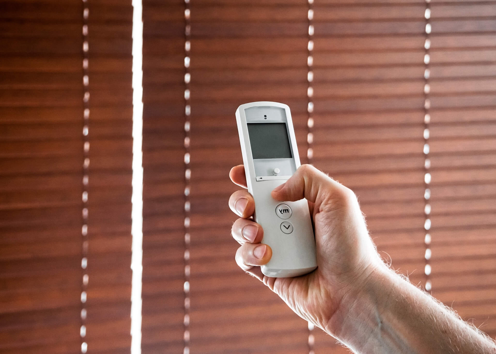 Hand holds a remote control to open the window blinds